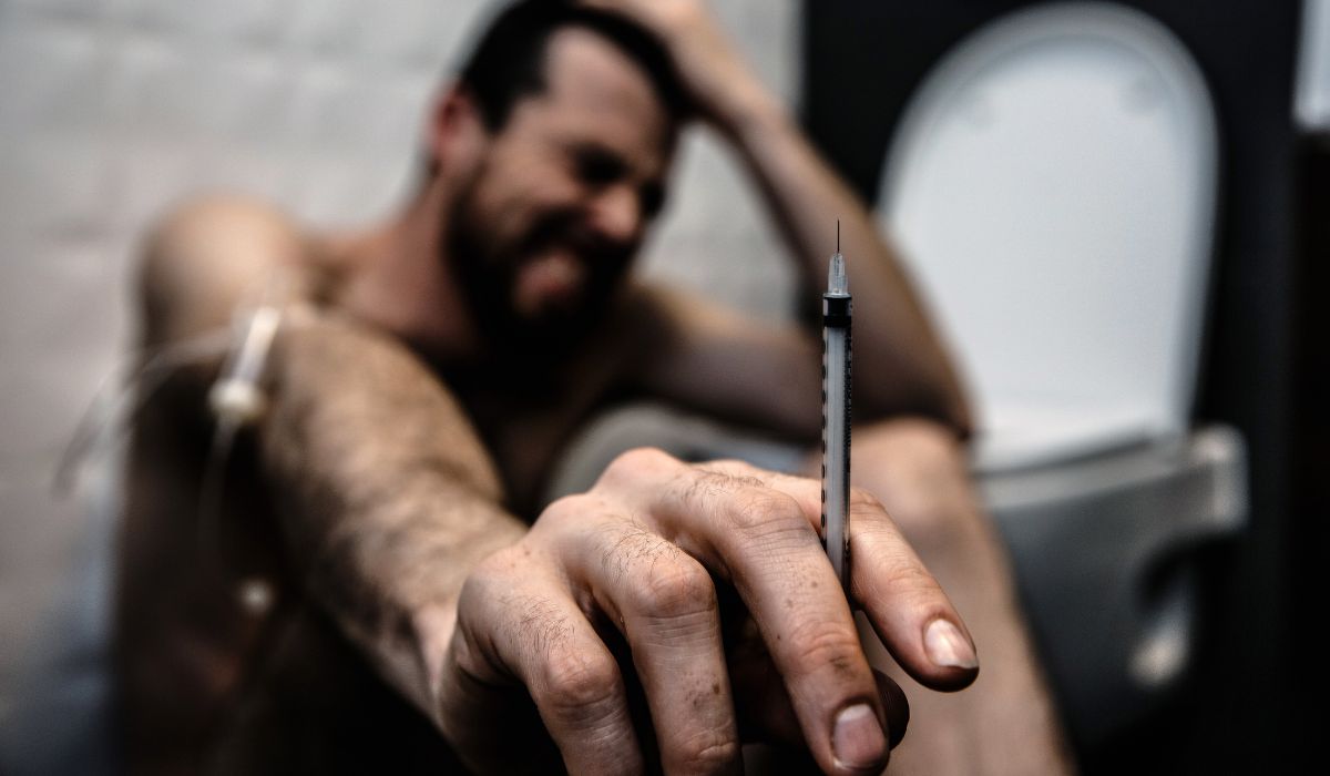 man using heroin and sitting against wall